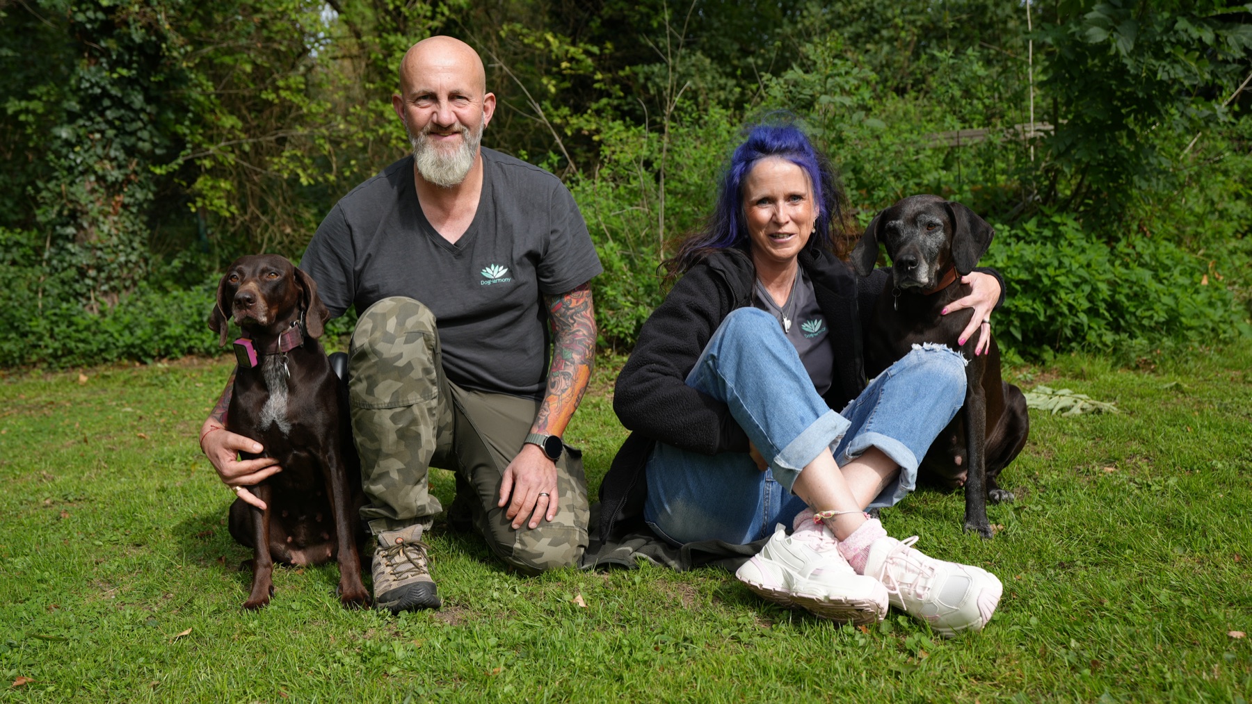 Zwei DogHarmony-Teammitglieder sitzen mit ihren Hunden im Grünen
